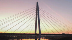 Cable-stayed bridge silhouetted against a dusky sky with golden and pink hues reflected in still water below.