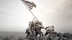 Soldiers raising an American flag on rocky terrain during overcast conditions.