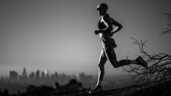 Silhouetted runner jogging on a ridge overlooking a hazy cityscape at dusk.