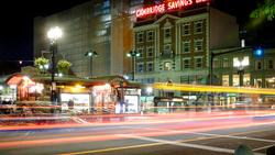 Night street scene with light trails from passing vehicles and illuminated historic buildings.