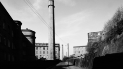 Industrial urban street with tall chimney and apartment buildings in black and white.