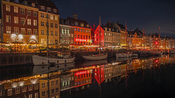 Historic waterfront at dusk with colorful buildings reflected in still water, illuminated by warm lights.