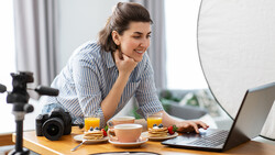 Content creator at desk with camera, ring light, laptop, and breakfast items during video recording setup.
