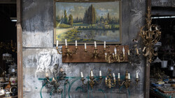 Weathered wall display with landscape painting, brass candelabras, and decorative sconces in vintage setting.