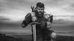 Bearded man in Viking-style armor holding a large sword against a cloudy landscape.