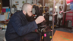 Photographer operating a large format camera mounted on a tripod in a studio setting.