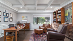 Home office with wood desk, leather seating, coffered ceiling, and built-in shelving.