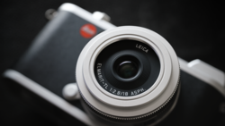Leica Elmarit lens on mirrorless camera body against dark background.