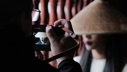 Cinematographer holding a professional video camera with monitor attachment in dark indoor venue.