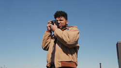 Photographer holding a camera up to his face while looking through the viewfinder against a clear blue sky.