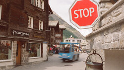 Alpine village street with red stop sign, motion-blurred vehicle, and traditional stone buildings.
