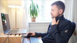 Man at desk reviewing laptop screen while working with keyboard and mouse in bright home office.