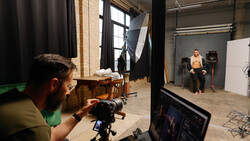 Photographer operating camera on tripod during studio shoot with model and lighting setup.