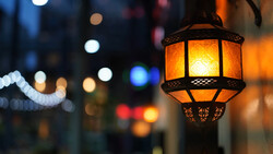 Ornate brass lantern with glowing amber glass panels hanging in an urban street at dusk.