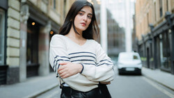 Young woman in striped sweater standing on urban street with classical architecture.