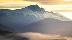 Layered mountain peaks bathed in golden sunrise light with misty valleys below.