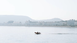 Small red boat on calm water with misty waterfront buildings in the background.