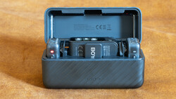 Open gray protective case containing a wireless microphone system with transmitter, receiver, and battery compartments on wooden surface.