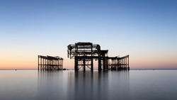 Silhouetted remains of a wooden pier structure at dusk, surrounded by still water.