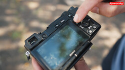 Hands holding a mirrorless camera displaying a blue-tinted live view on its rear LCD screen.