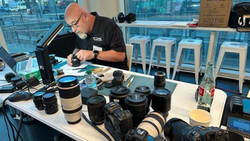 Photographer reviewing camera lenses and equipment at a desk in a high-rise office with city views.