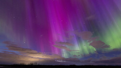 Aurora borealis display with vibrant magenta and green bands arcing across a twilight sky above a dark landscape.