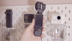 Hand holding a compact gimbal-stabilized camera with articulating head and small screen display.