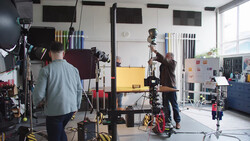 Professional film or photo production studio with crew operating camera equipment and lighting rigs during an active shoot.