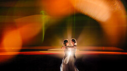 Couple dancing silhouetted against warm orange and golden bokeh light backdrop.