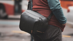 Person wearing a black camera backpack with shoulder strap over casual clothing in an urban street setting.