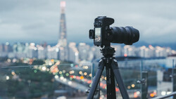 Professional camera on tripod mounted on elevated vantage point overlooking cityscape at dusk.