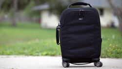 Black carry-on luggage with spinner wheels positioned on a driveway with residential setting in background.