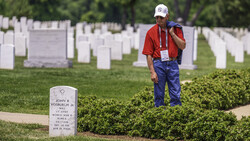 Man in red shirt and blue pants standing among white military headstones in a cemetery.