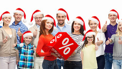 Group of diverse people wearing Santa hats holding a red discount sign with percentage symbols.