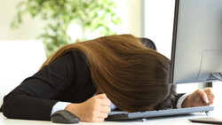 Person slumped over desk with head resting on keyboard, displaying exhaustion or burnout.