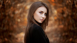 Young woman with long dark hair gazing over her shoulder against a blurred autumn forest background.