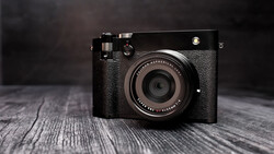 Black rangefinder camera with textured leather body on weathered wooden surface.