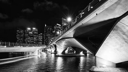 Modern bridge underpass with curved concrete architecture and illuminated city skyline at night.