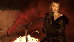 Woman singing at microphone with dramatic red and orange lighting and smoke effects.