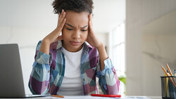 Person holding head with hands while looking down at laptop, showing signs of stress or concentration.
