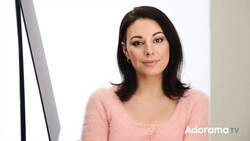 Woman with dark shoulder-length hair wearing a pink cardigan, looking at camera in a bright studio setting.