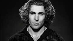 Black and white portrait of a man with shoulder-length curly hair and a chain necklace.