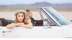 Bride with baby's breath crown leaning out of vintage convertible car door.