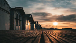 Row of beach huts stretching into distance under golden sunset sky with dramatic clouds.