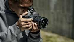 Young photographer holding a DSLR camera with telephoto lens while composing a shot outdoors.