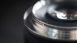 Close-up of a camera lens with selective focus, showing metal barrel and glass elements with shallow depth of field.