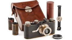 Vintage Leica rangefinder camera with leather case and accessories arranged on white background.