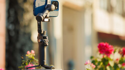 Smartphone mounted on a gimbal stabilizer with pink flowers in soft focus background.