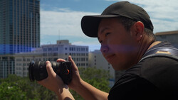 Photographer using binoculars on an urban rooftop with cityscape in background.