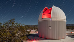 Observatory dome with open slot revealing illuminated red telescope against star trail sky.